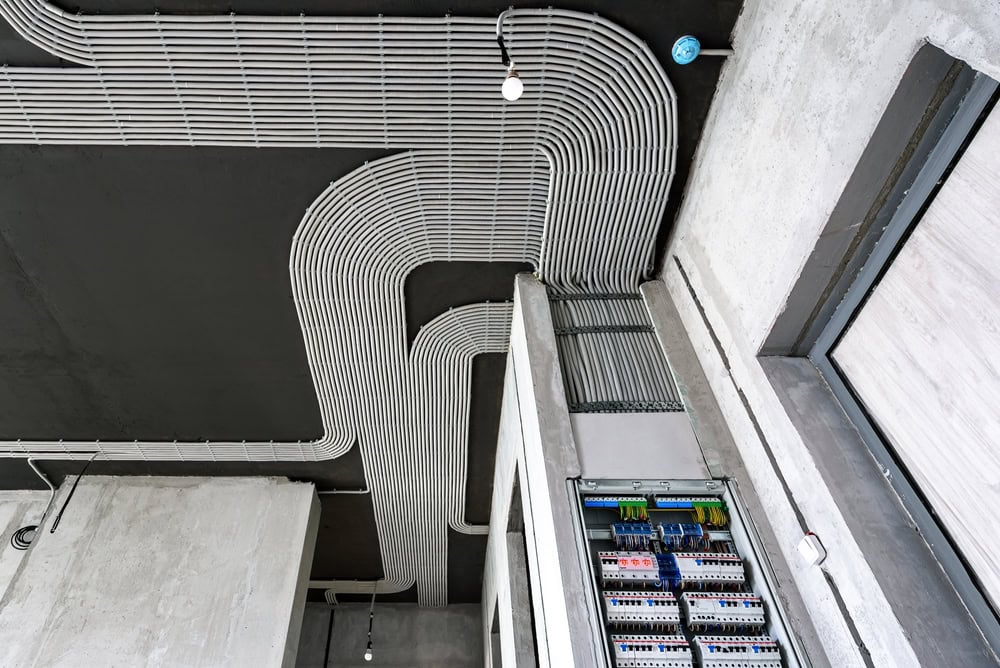 Electrical cables and switch box on house concrete ceiling and wall. Modern plastic hoses with wires in room. Lines of pvc wiring tubes after professional work. Renovation of home or factory interior